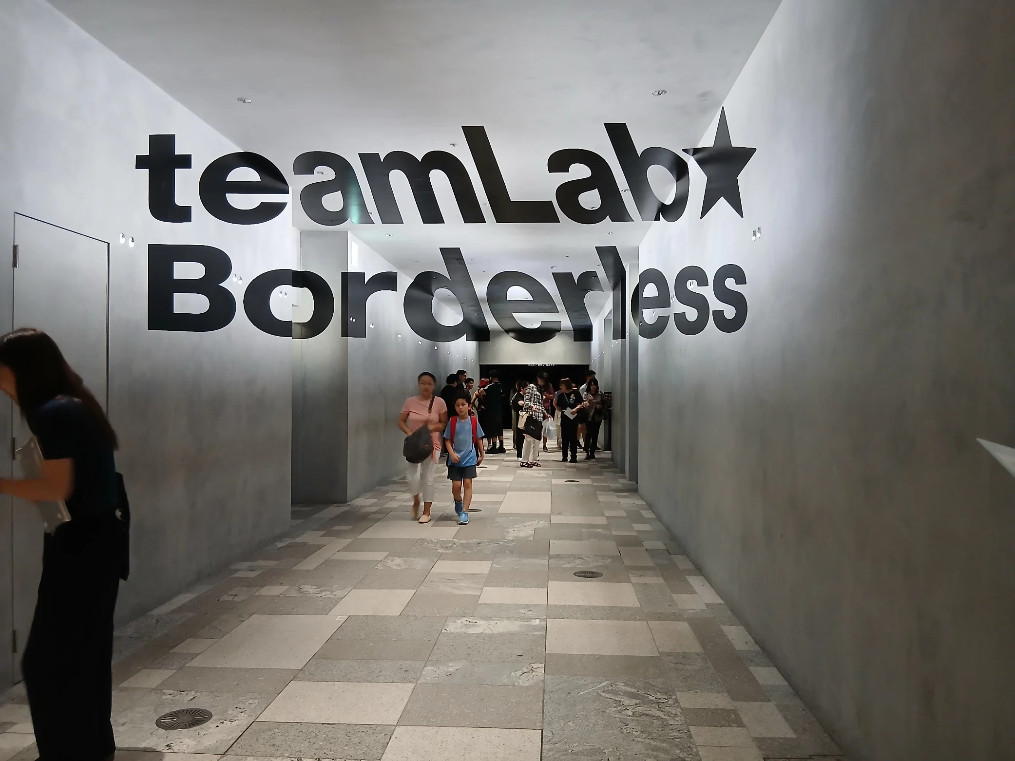 チームラボボーダレス麻布台ヒルズの入口。teamLab Borderlessのロゴが掲げられた通路を歩く来館者